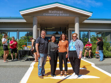 1 man and 3 female leadership team members pose in front of elementary school and on new orange crosswalk