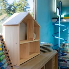 Wooden doll house sitting on a bookcase with a spiral metal play equipment in the background