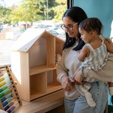 Mother holding their young child in their arms while looking at toys.