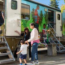 An adult woman greets other adults and kids as they walk into a transform RV for reading and playing.