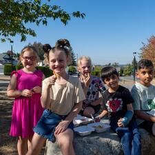 Small group of elementary students sitting on a rock, eating french fries.